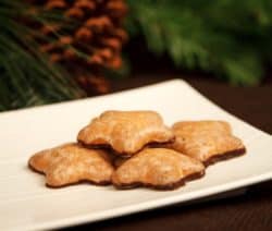 Fünf sternförmige Lebkuchen auf einem weißen Teller, Tannenzweige im Hintergrund.