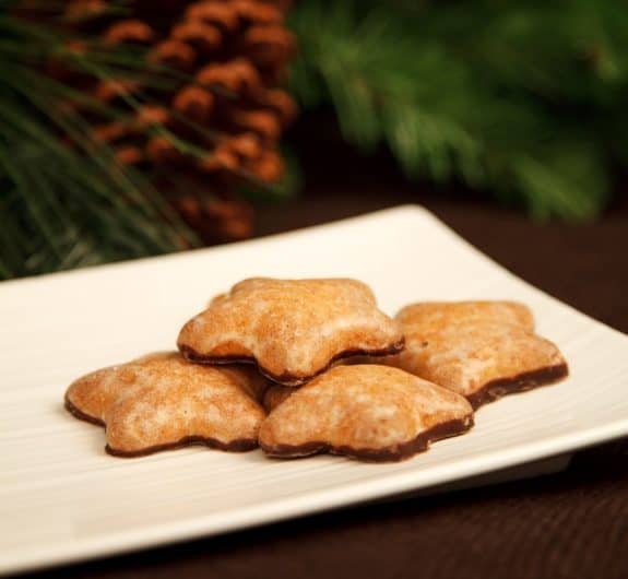 Fünf sternförmige Lebkuchen auf einem weißen Teller, Tannenzweige im Hintergrund.