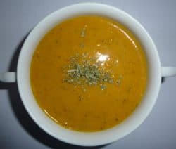 Eine weiße Schale mit orangefarbener Suppe, garniert mit getrockneten Kräutern.