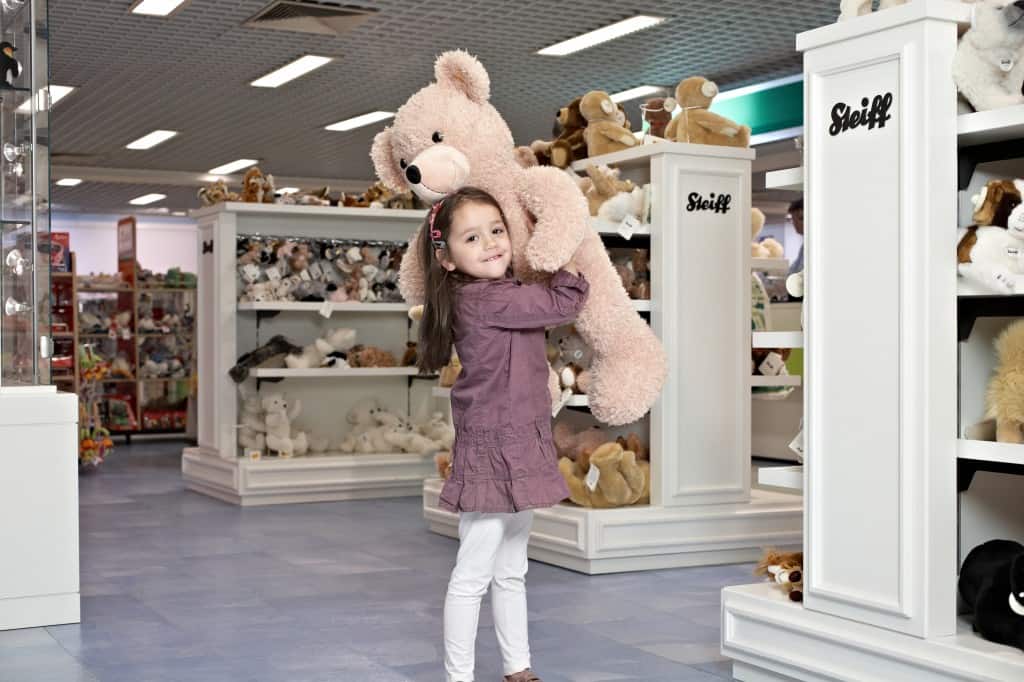 Ein Mädchen hält einen großen, flauschigen Teddybären in einem Spielzeugladen.
