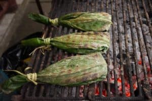 Drei in Bananenblätter gewickelte Päckchen liegen auf einem Grillrost über glühenden Kohlen.