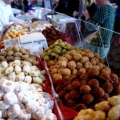 Ein Marktstand mit verschiedenen Keksen, Menschen stehen davor und wählen aus.