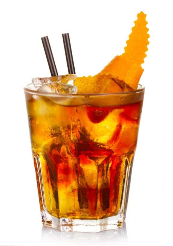 Ein Cocktailglas mit Eis, zwei schwarzen Strohhalmen und einer Orangenschale.