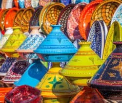 Bunte, verzierte Tajine-Töpfe in verschiedenen Farben und Mustern auf einem Markt ausgestellt.