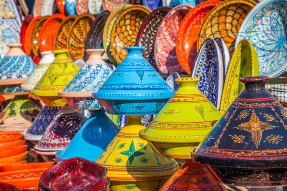 Bunte, verzierte Tajine-Töpfe in verschiedenen Farben und Mustern auf einem Markt ausgestellt.
