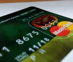Grüne Debitkarte mit Mastercard-Logo und geprägten Zahlen auf weißem Hintergrund.
