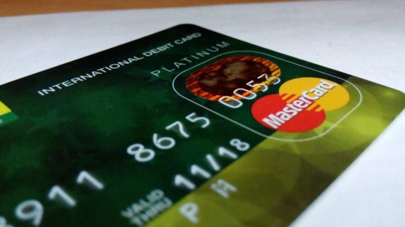 Grüne Debitkarte mit Mastercard-Logo und geprägten Zahlen auf weißem Hintergrund.
