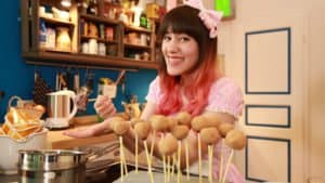 Frau in rosa Kleid dekoriert Cake Pops in einer Küche.