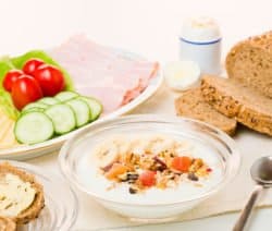 Ein Frühstückstisch mit Müsli, Brot, Aufschnitt, Käse, Tomaten und Gurken.