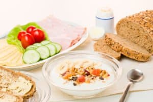 Ein Frühstückstisch mit Müsli, Brot, Aufschnitt, Käse, Tomaten und Gurken.