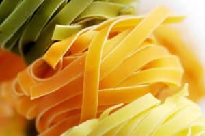 Bunte Bandnudeln in Grün, Orange und Gelb sind eng aufgerollt und liegen nebeneinander.