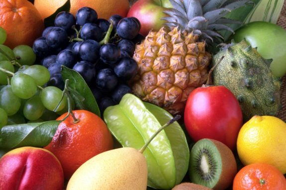 Verschiedene Früchte wie Ananas, Trauben, Kiwi und Orangen liegen dicht beieinander.