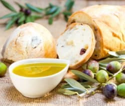 Brot, Olivenöl und Oliven auf Sackleinen, umgeben von Olivenzweigen.