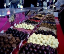 Eine bunte Auswahl an Pralinen auf einem Marktstand mit rotem Tisch und vielen Besuchern im Hintergrund.