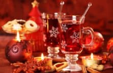Zwei Gläser Glühwein mit Schneeflockenmuster, umgeben von Kerzen, Keksen und Weihnachtsdekoration.