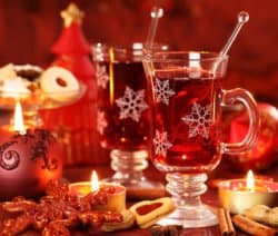Zwei Gläser Glühwein mit Schneeflockenmuster, umgeben von Kerzen, Keksen und Weihnachtsdekoration.