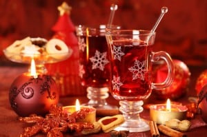 Zwei Gläser Glühwein mit Schneeflockenmuster, umgeben von Kerzen, Keksen und Weihnachtsdekoration.