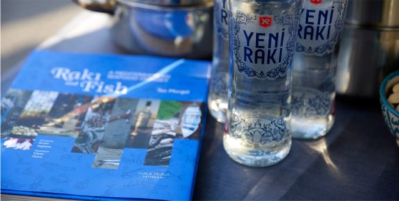 Buch 'Raki and Fish' neben zwei Yeni Raki-Flaschen auf einem Tisch.