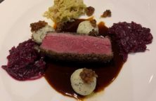 Ein Stück rosa gebratenes Fleisch mit Rotkohl, Sahnekugeln und Soße auf einem weißen Teller.