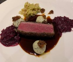 Ein Stück rosa gebratenes Fleisch mit Rotkohl, Sahnekugeln und Soße auf einem weißen Teller.