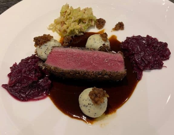 Ein Stück rosa gebratenes Fleisch mit Rotkohl, Sahnekugeln und Soße auf einem weißen Teller.
