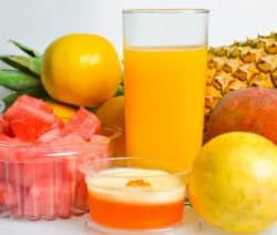 Ein Glas Orangensaft, Ananas, Mango, Melonenstücke und eine Zitrone auf weißem Hintergrund.