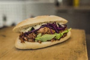 Ein Sandwich mit Pulled Pork, Rotkohl und Rucola auf einem Holzbrett.