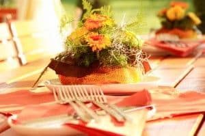 Blumenarrangement mit gelben und orangefarbenen Blüten auf einem gedeckten Tisch mit orangefarbenen Servietten und Besteck.