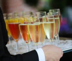Ein Kellner serviert ein Tablett mit gefüllten Champagnergläsern in verschiedenen Farben.