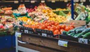 Frische Tomaten und Gurken in Holzkisten in einem Supermarkt, im Hintergrund unscharfes Obst und Gemüse.