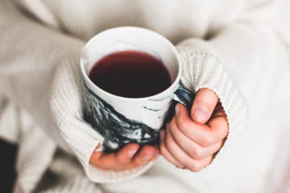 Hände in Strickpullover halten eine Tasse mit rotem Tee.