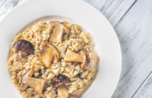 Ein Teller mit Pilzrisotto auf einem hellen Holztisch.