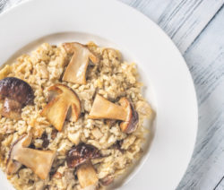 Ein Teller mit Pilzrisotto auf einem hellen Holztisch.