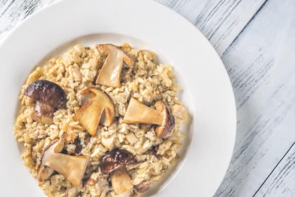 Ein Teller mit Pilzrisotto auf einem hellen Holztisch.