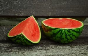 Eine halbe und eine Scheibe Wassermelone auf einer Holzbank.