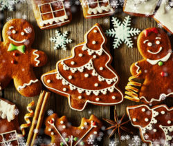 Lebkuchenfiguren und Tannenbaumkekse auf Holztisch, umgeben von Schneeflocken und Gewürzen.