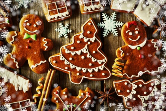 Lebkuchenfiguren und Tannenbaumkekse auf Holztisch, umgeben von Schneeflocken und Gewürzen.