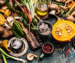 Frisches Gemüse, Pilze, Kürbis, Ölflasche und Gewürze auf rustikalem Tisch angeordnet.