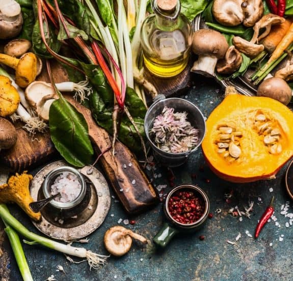 Frisches Gemüse, Pilze, Kürbis, Ölflasche und Gewürze auf rustikalem Tisch angeordnet.