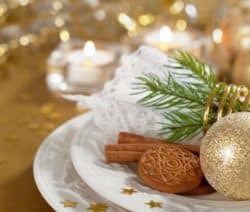 Ein Weihnachtsteller mit Zimtstangen, Keksen, Tannenzweig und goldener Kugel, umgeben von Kerzenlicht und goldenen Sternen.